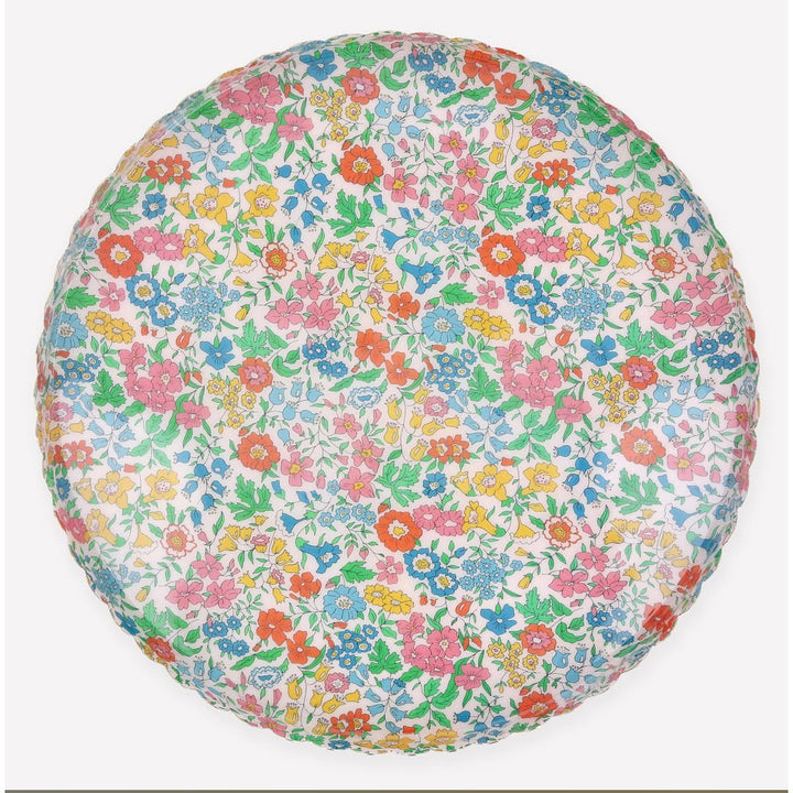 A round decorative cushion or pillow featuring a dense, all-over floral print with red, pink, blue, yellow, and green flowers on a white background, shown against a light gray studio backdrop.