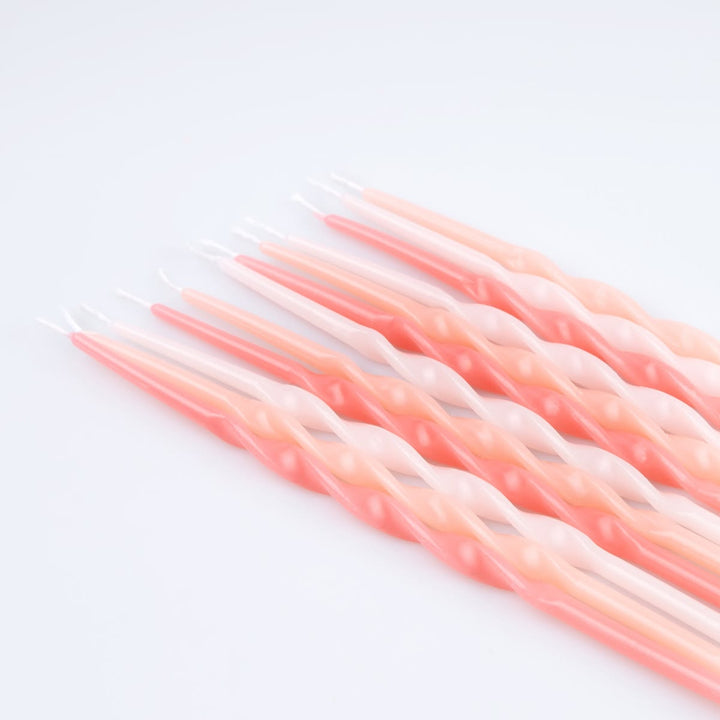 A set of twisted taper candles in a soft pink and peach gradient, arranged diagonally on a clean white background.