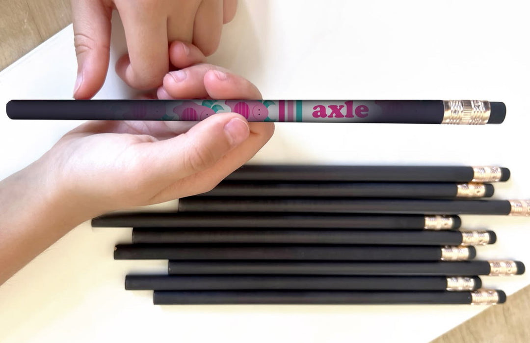 Person holding a set of black pencils with decorative ends on a white background