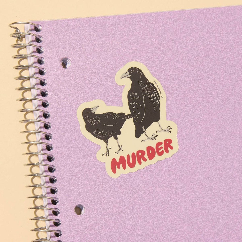 Notebook with a sticker of two crows and the word 'MURDER' on a purple cover.
