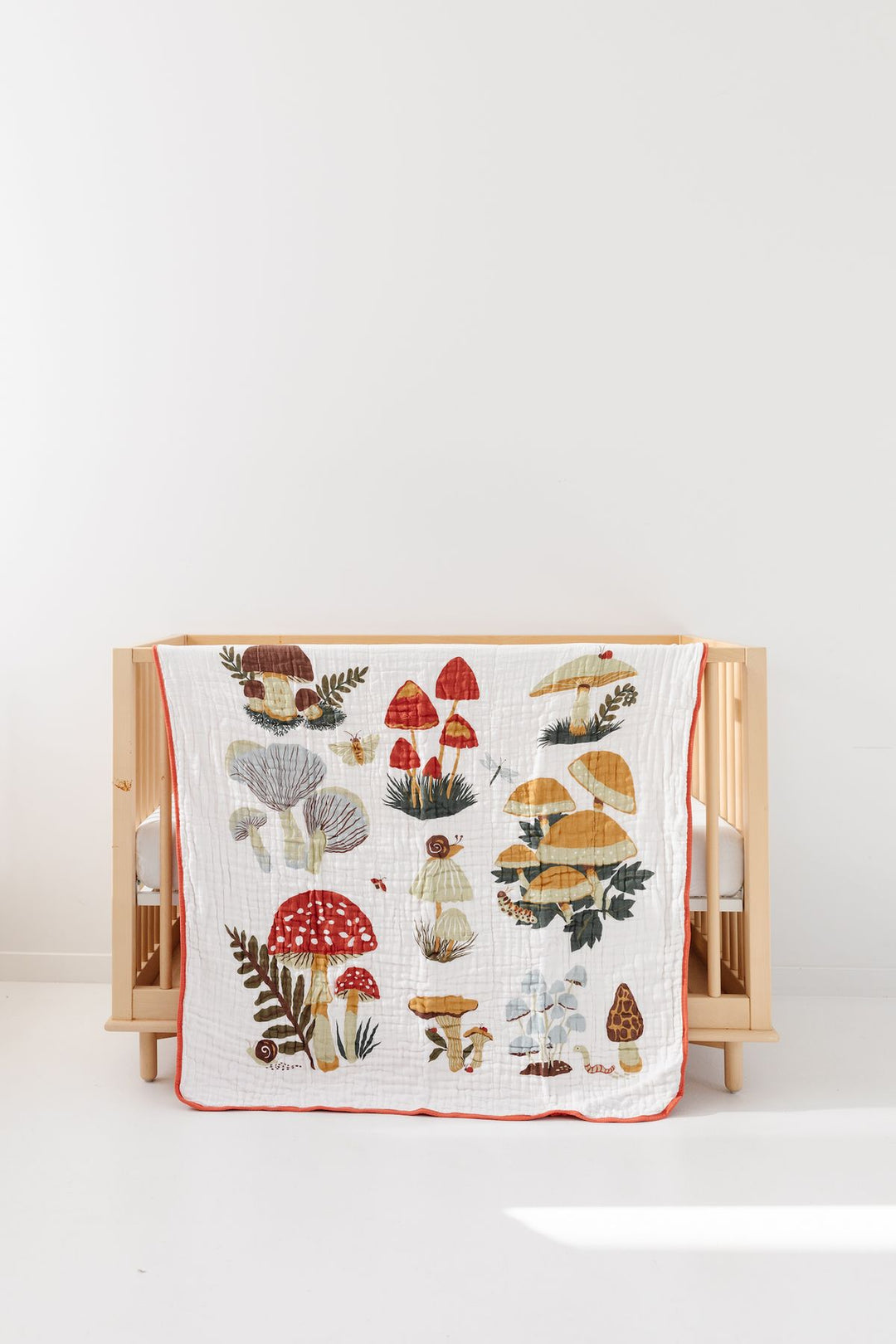 Baby crib with a mushroom-themed quilt on a white background