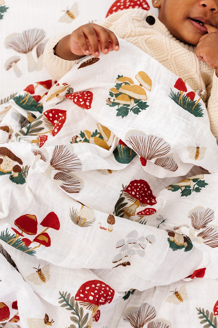 Baby wrapped in a blanket with a forest-themed pattern, surrounded by Christmas decorations.