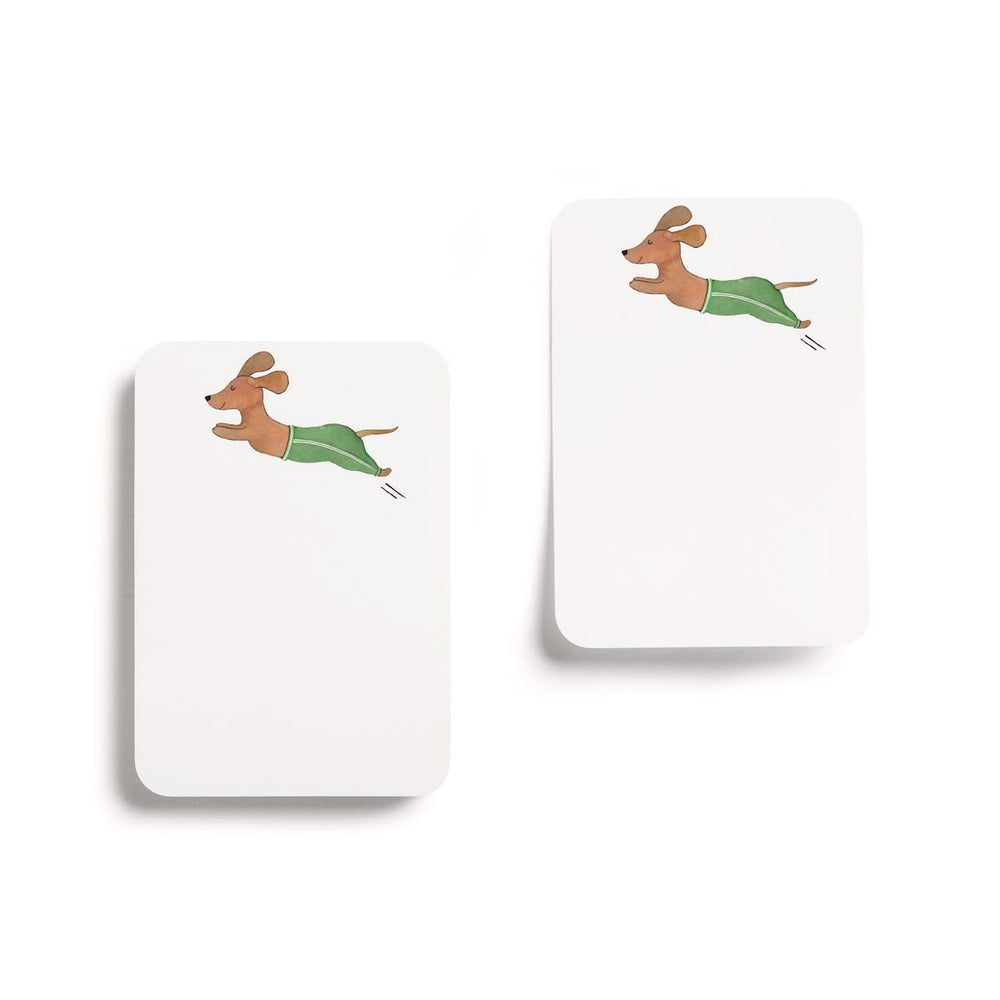 Two white rectangular cards or tags with rounded corners, each printed with a small illustration of a brown dachshund wearing green pants, shown on a clean white background.