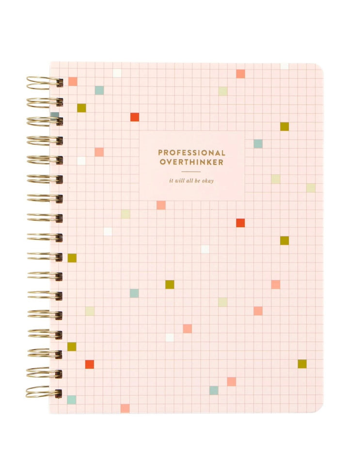 A spiral-bound notebook with a light pink grid cover, featuring small scattered colored squares in red, orange, green, and blue, with the text 'PROFESSIONAL OVERTHINKER' and 'it will all be okay' printed on the front.