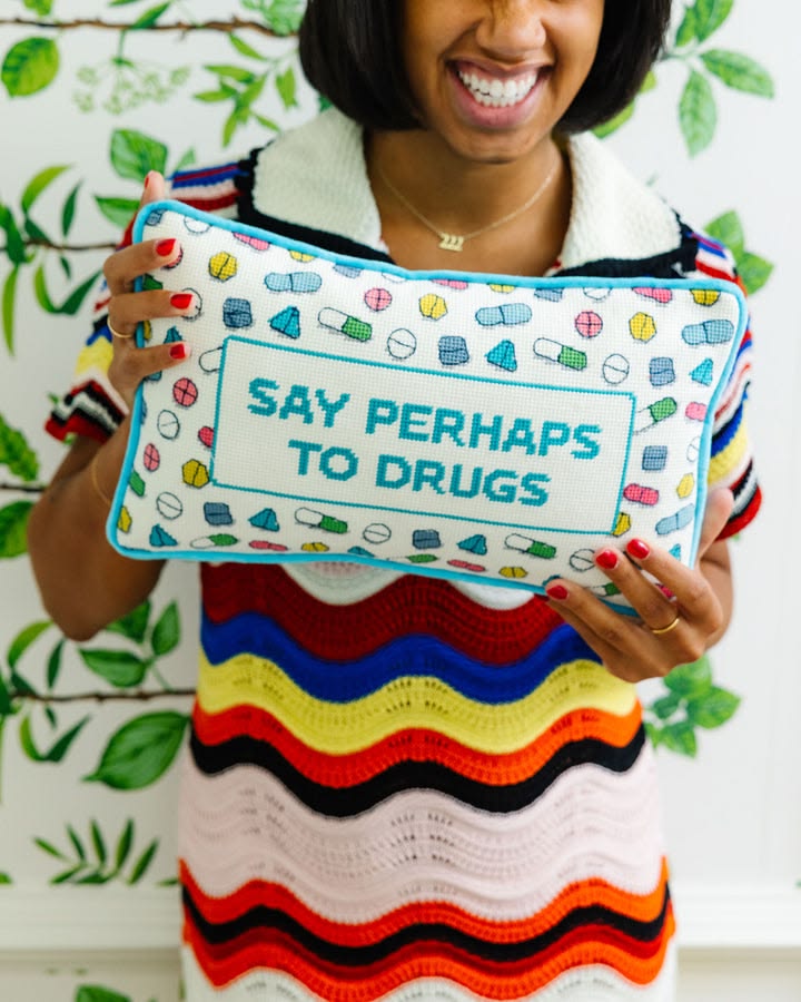 Person holding a pillow with 'Say Perhaps to Drugs' text against a green leafy background