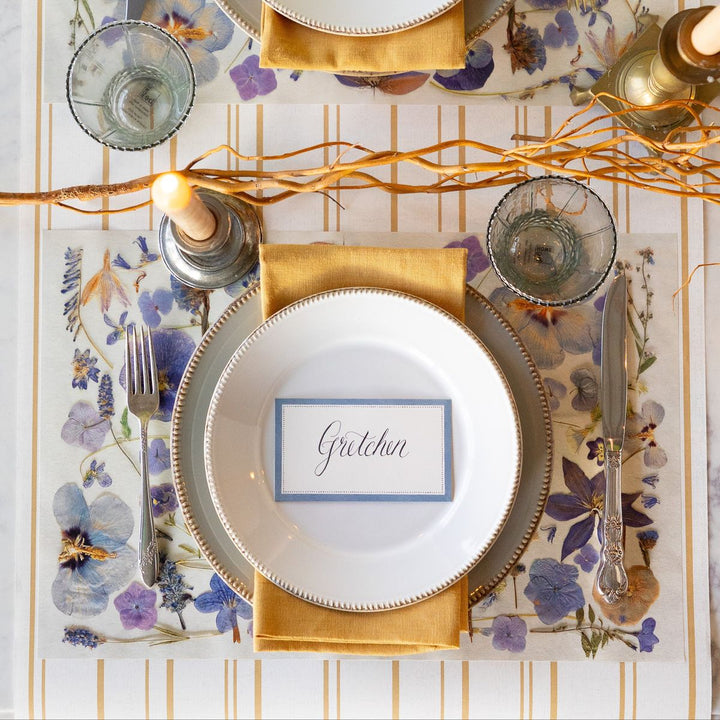 Elegant table setting with floral placemats, gold napkins, and decorative plates.