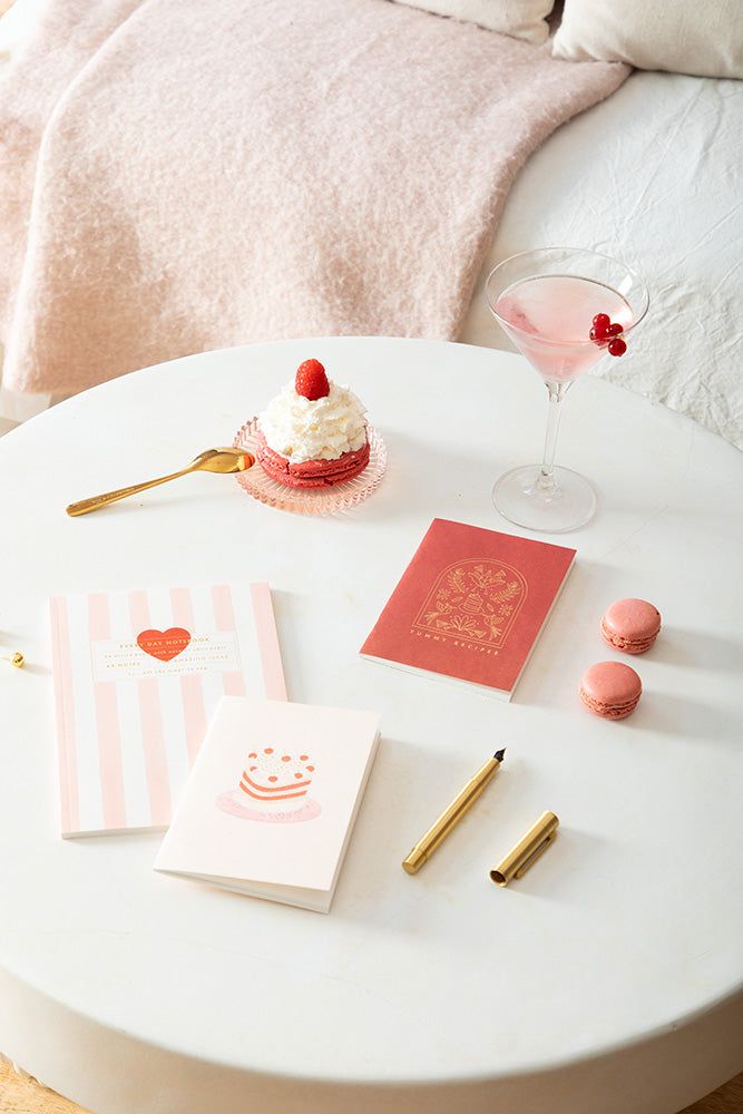 Table setting with a dessert, cocktail, and stationery items on a white surface.