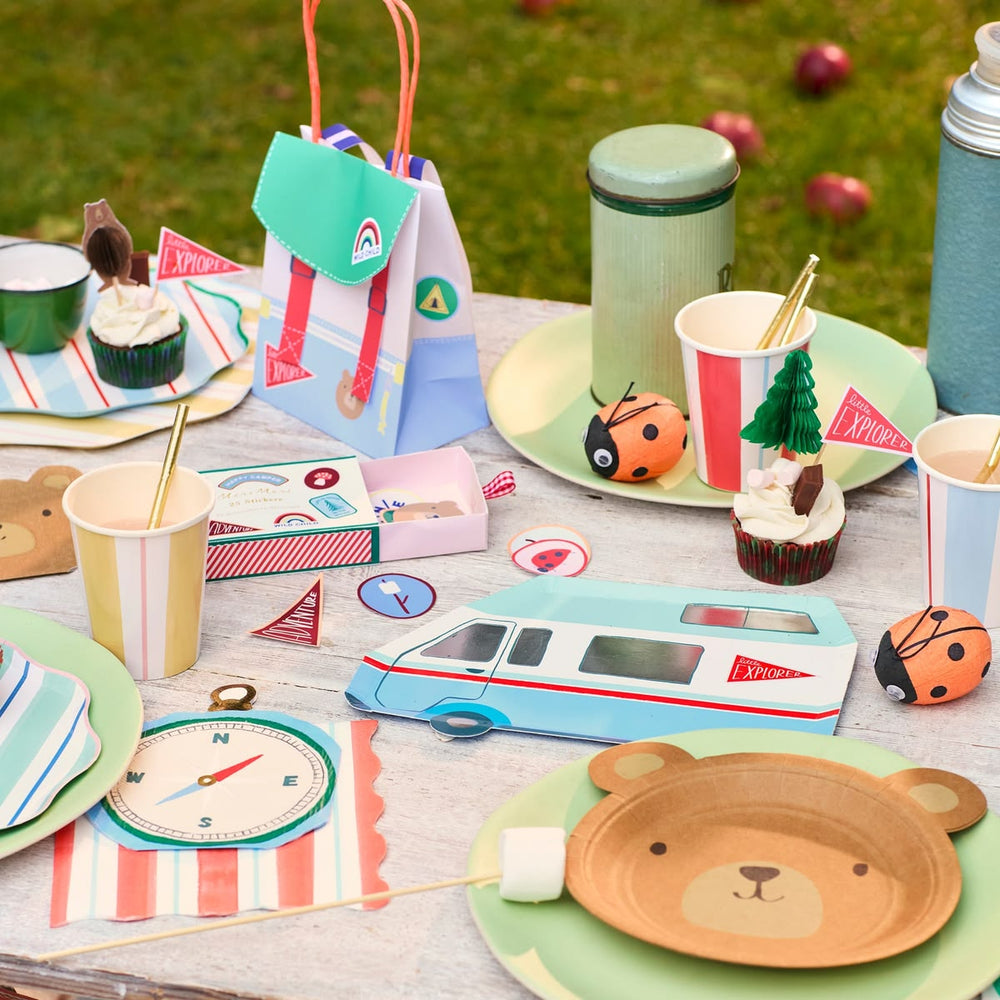 Children's party table setting with colorful plates, cups, and toys outdoors.