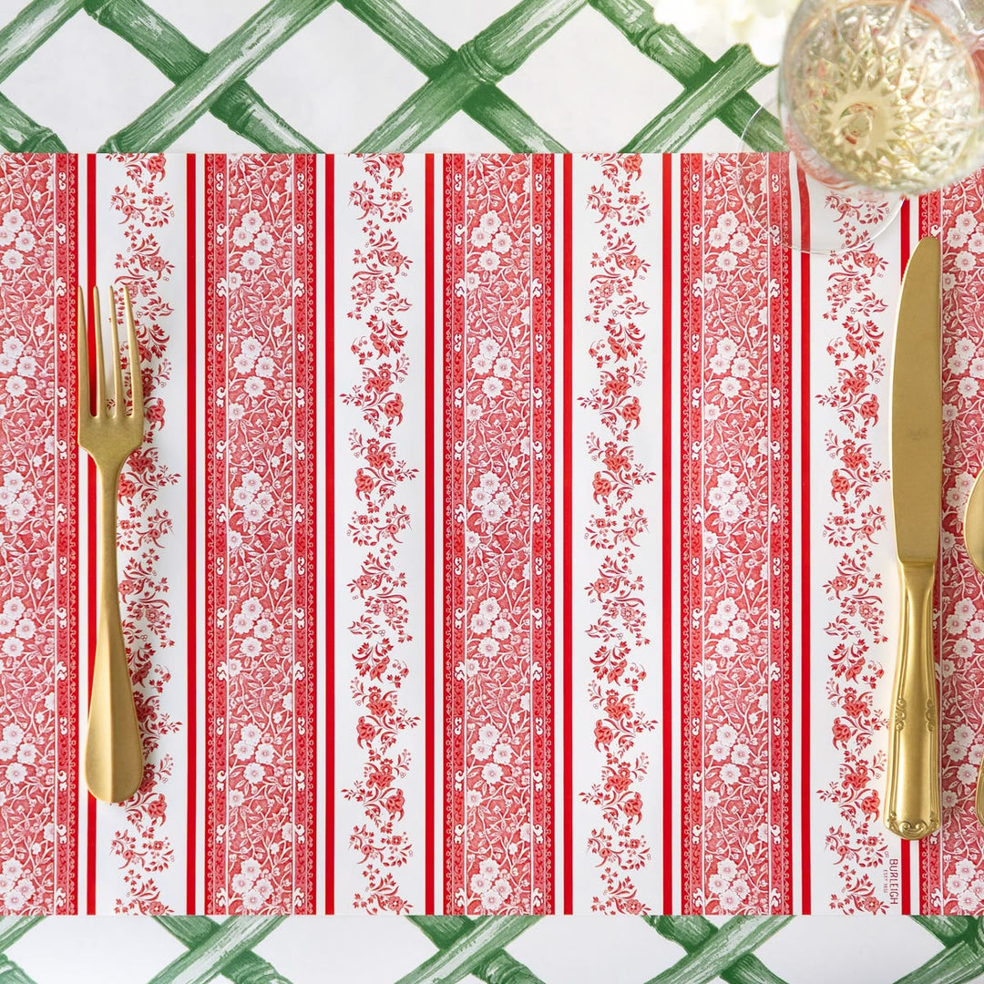 Patterned tablecloth with red and white stripes and floral designs, accompanied by gold cutlery.