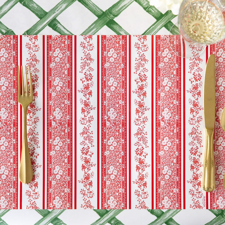 Patterned tablecloth with red and white stripes and floral designs, accompanied by gold cutlery.