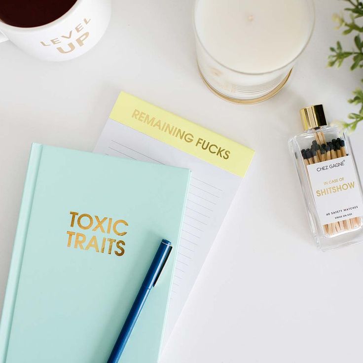 Notebooks with humorous titles, a candle, and a small bottle on a light surface.
