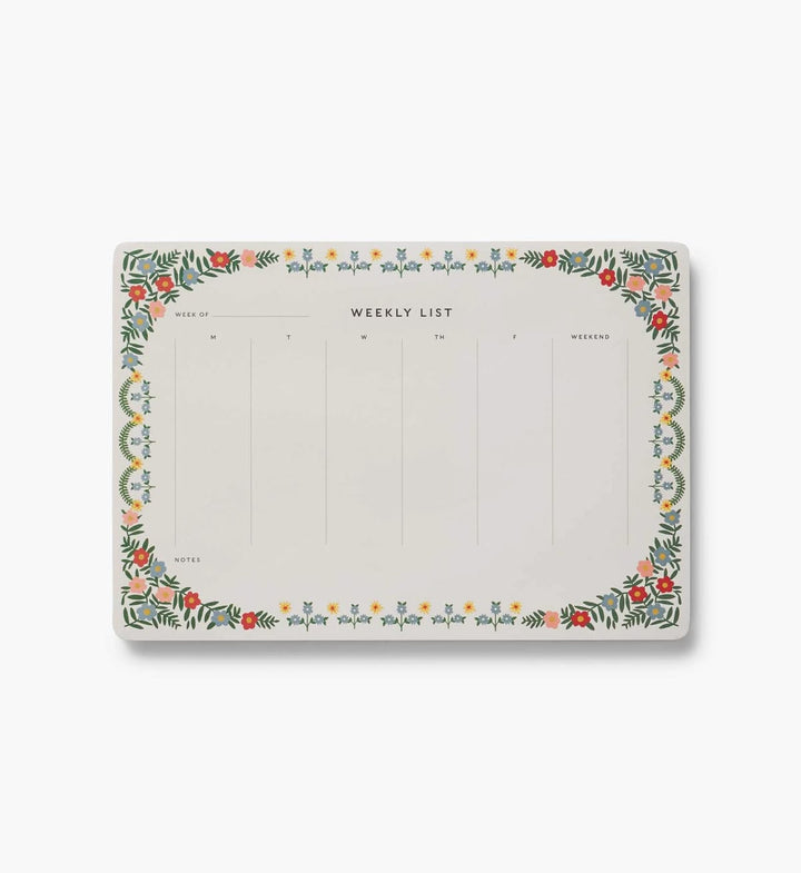 A weekly planner notepad with a decorative botanical border in green, red, orange, and yellow on a white background, shown on a light gray studio background.