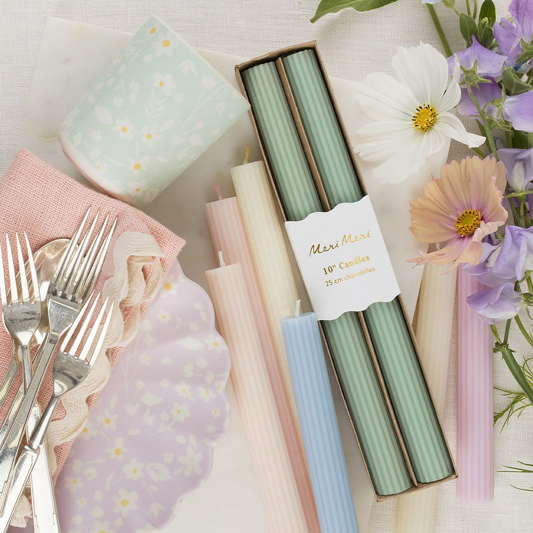 Pastel-colored candles in a box with floral and silverware accents on a light background