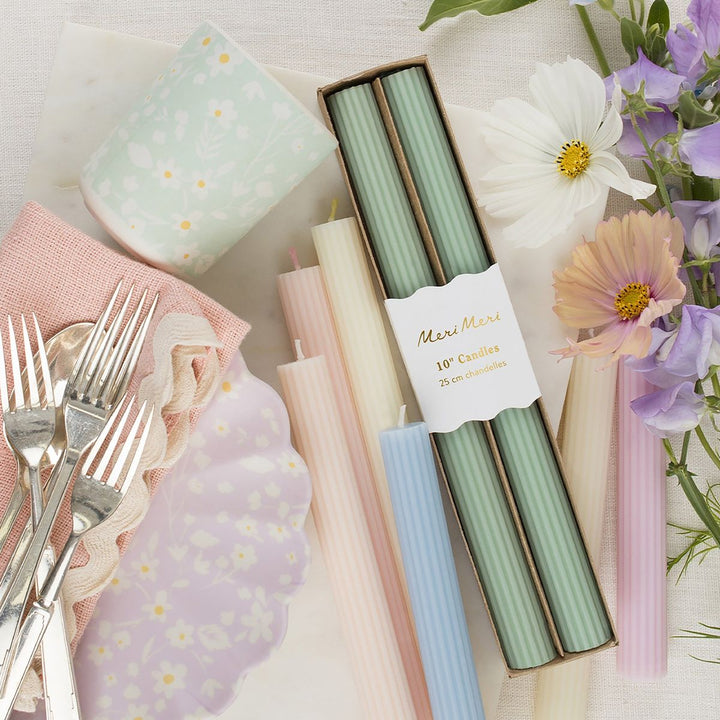 Pastel-colored candles in a box with floral and silverware accents on a light background