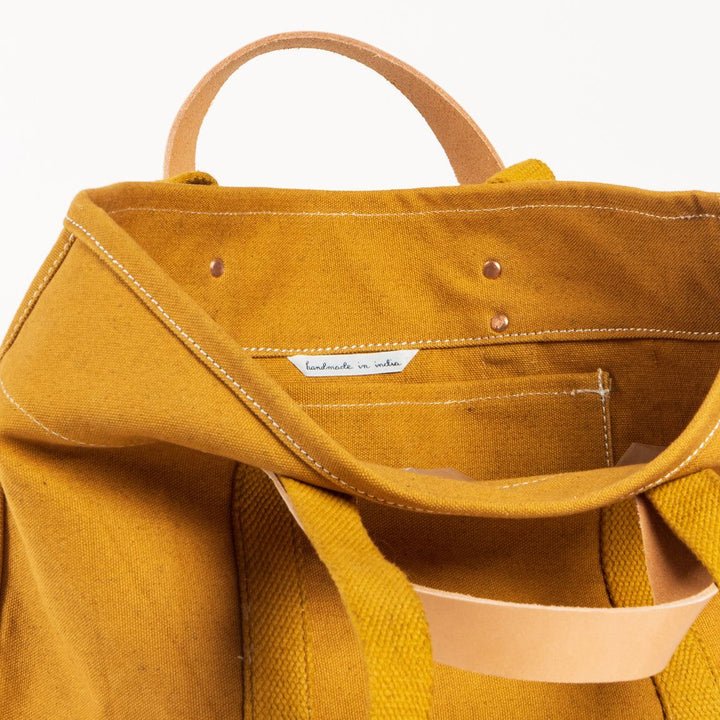 Close-up of a mustard yellow bag with visible stitching and brand label on a white background