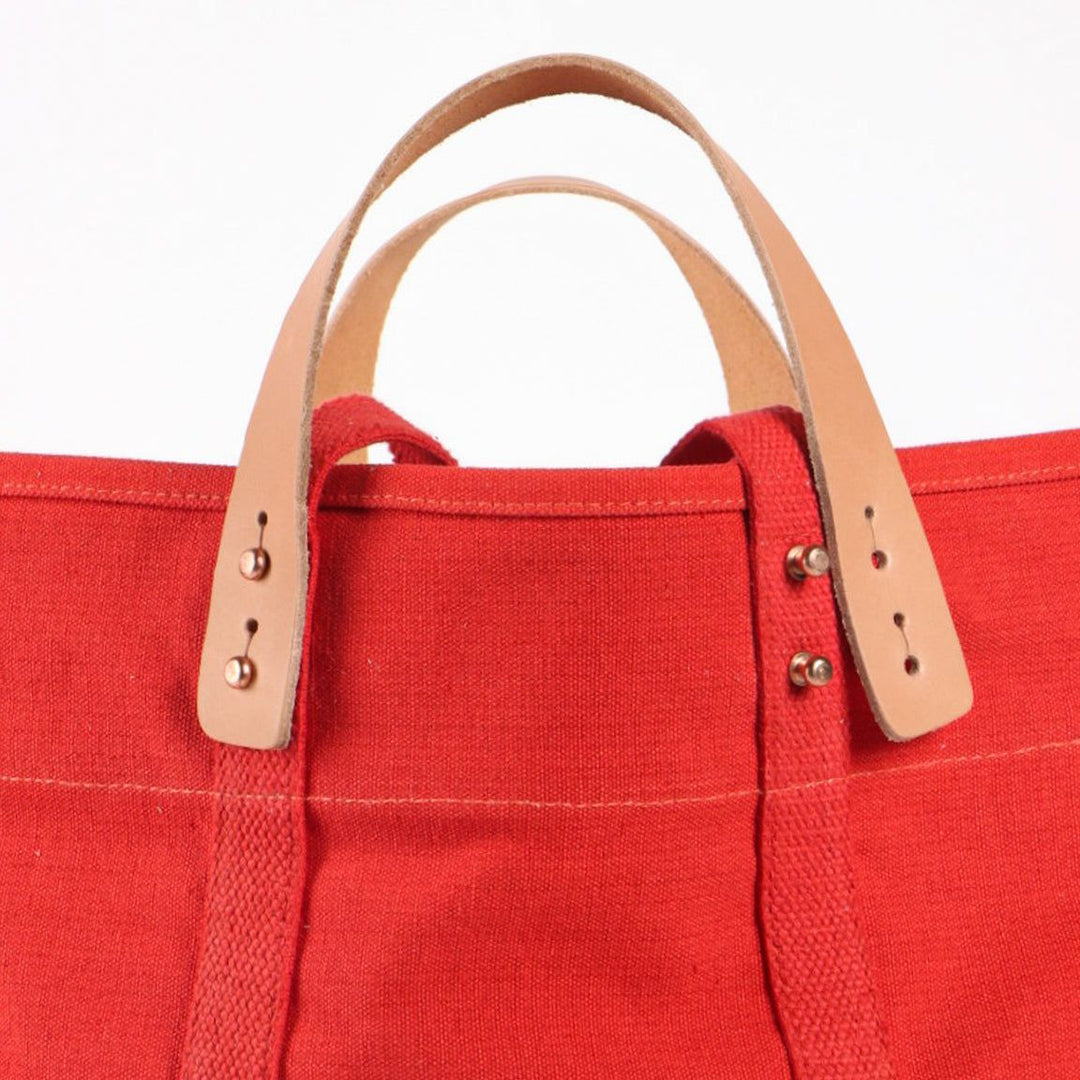 Red tote bag with brown leather handles on a white background