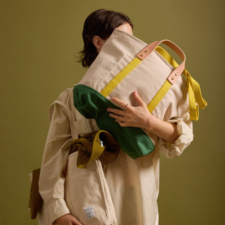 Person holding a large green bag with multiple straps against a solid background