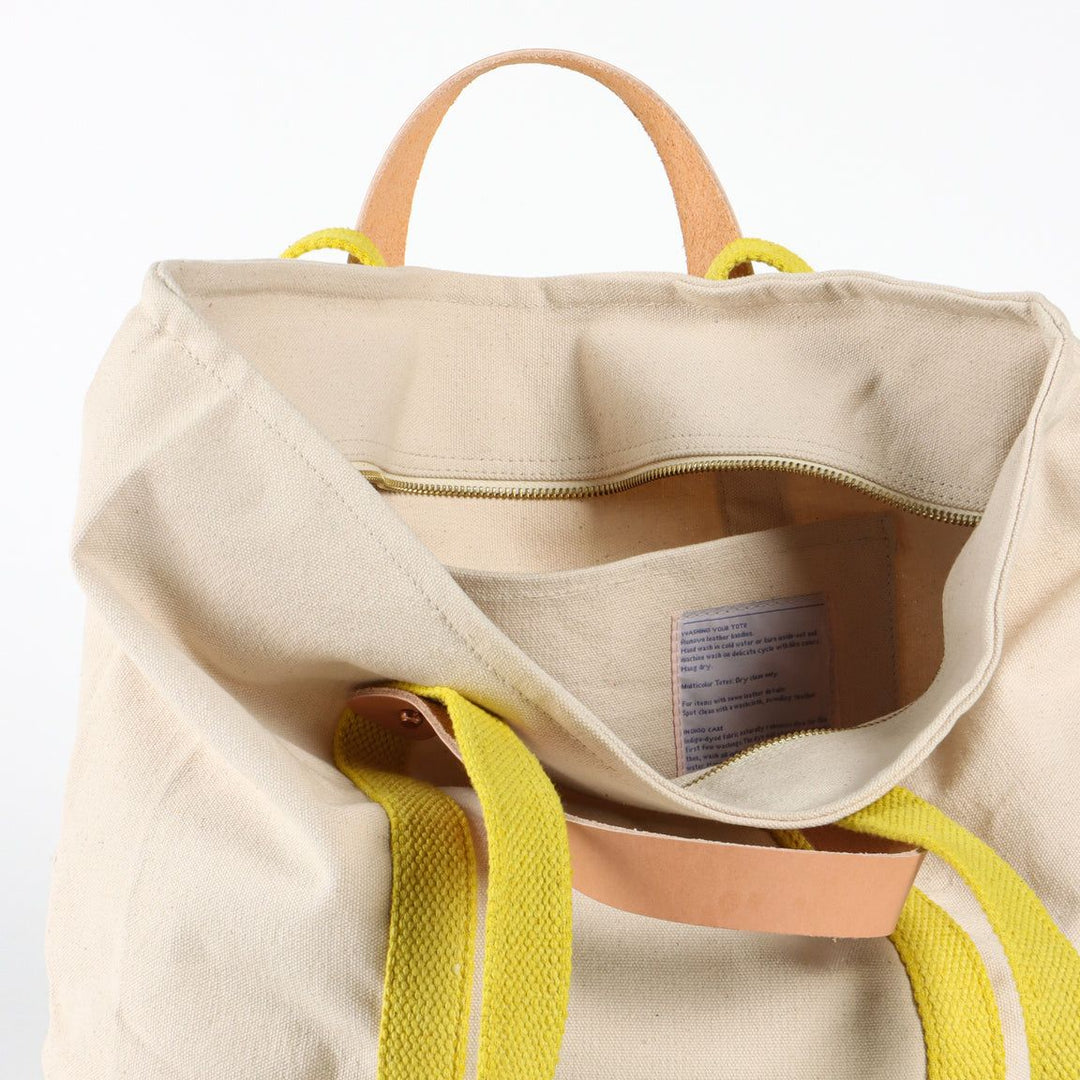 Beige tote bag with yellow straps and handles on a white background