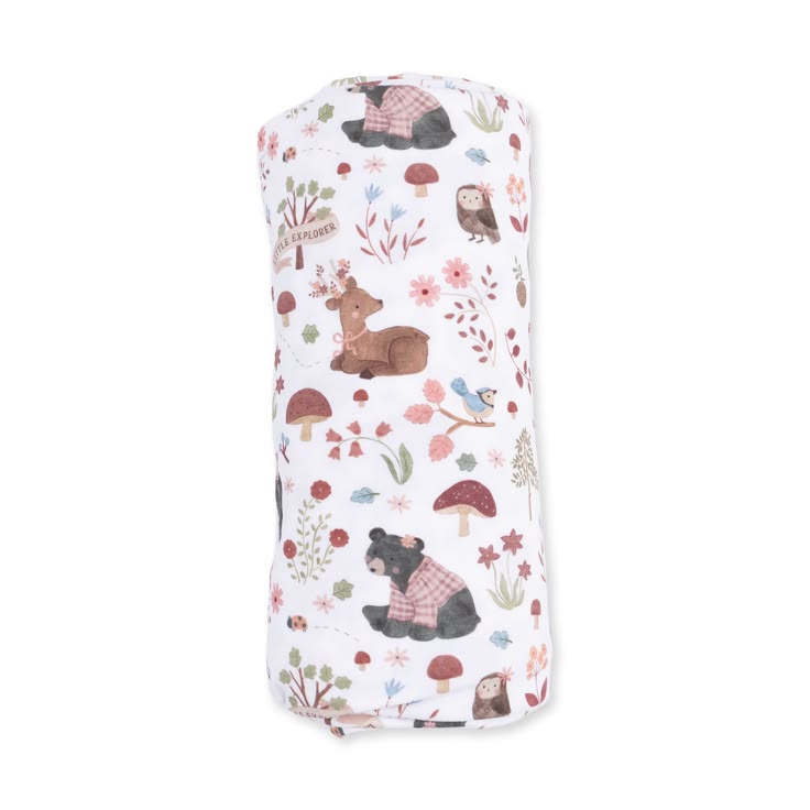 A rolled-up white muslin blanket featuring a whimsical forest pattern with brown deer, black bears in plaid sweaters, red mushrooms, and small birds, shown against a plain white background.