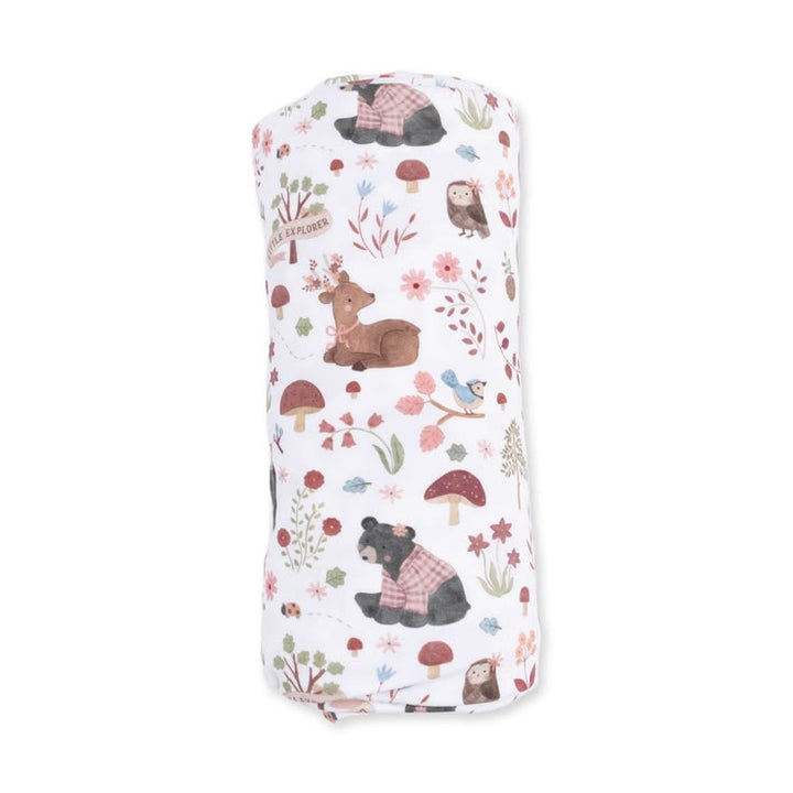 A rolled-up white muslin blanket featuring a whimsical forest pattern with brown deer, black bears in plaid sweaters, red mushrooms, and small birds, shown against a plain white background.