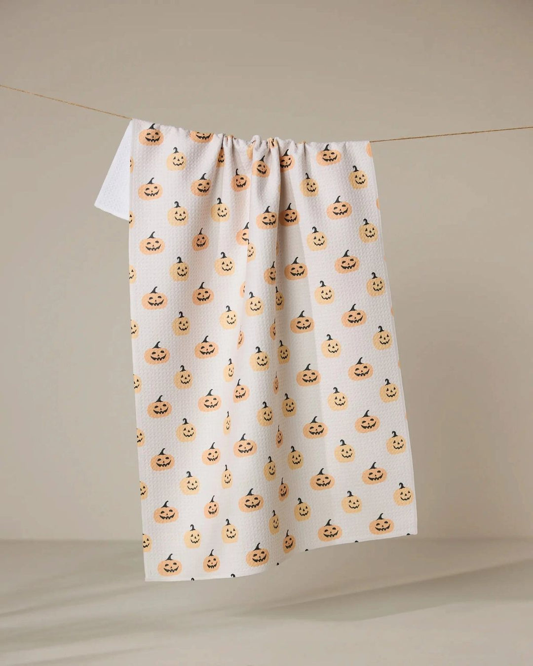 White towel with Halloween-themed jack-o'-lantern pattern hanging on a line against a beige background