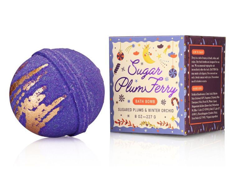 Purple bath bomb with gold glitter next to its packaging on a white background