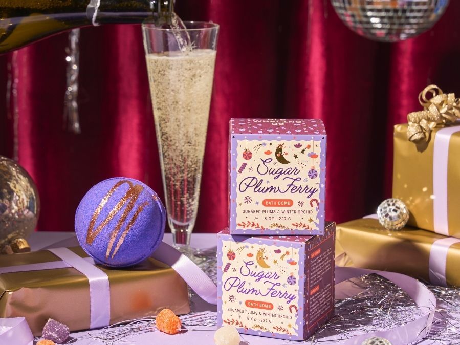 Two boxes of 'Sugar Plum Fairy' bath bombs on a festive table with champagne and gift boxes.