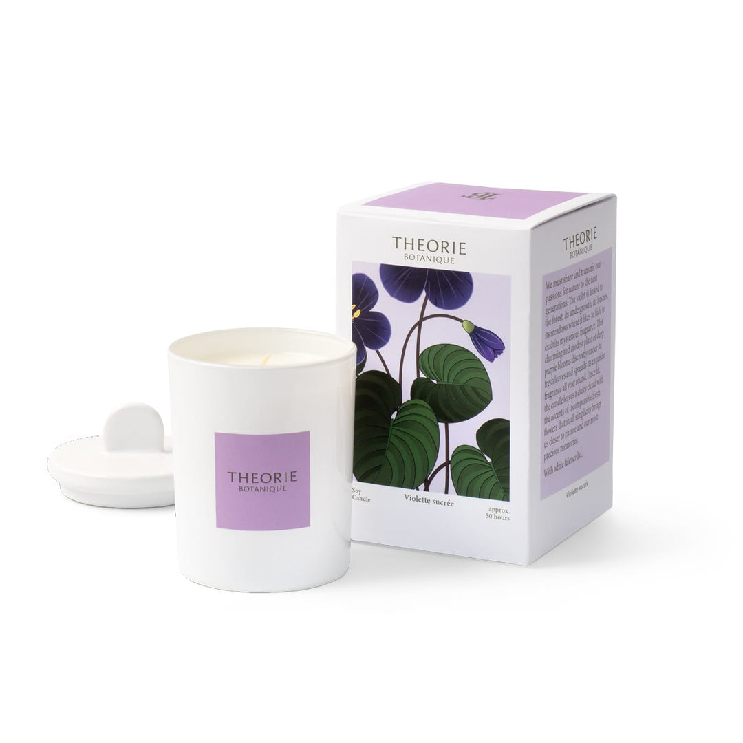 A white jar candle with a lavender label next to its matching white and lavender packaging box, both featuring a botanical illustration of purple flowers and green leaves. The brand name 'THEORIE BOTANIQUE' is visible on both the candle and the box.