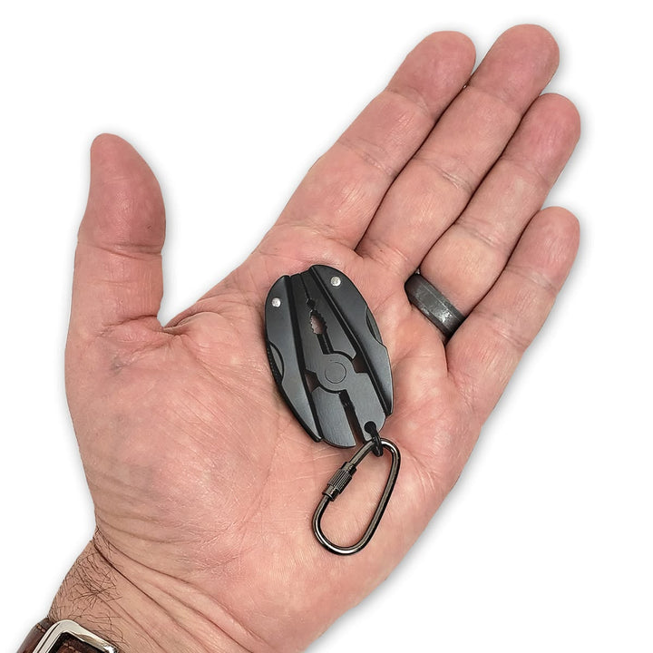 A black multi-tool pocket knife with a carabiner clip, held in the center of an open hand to show its small scale.