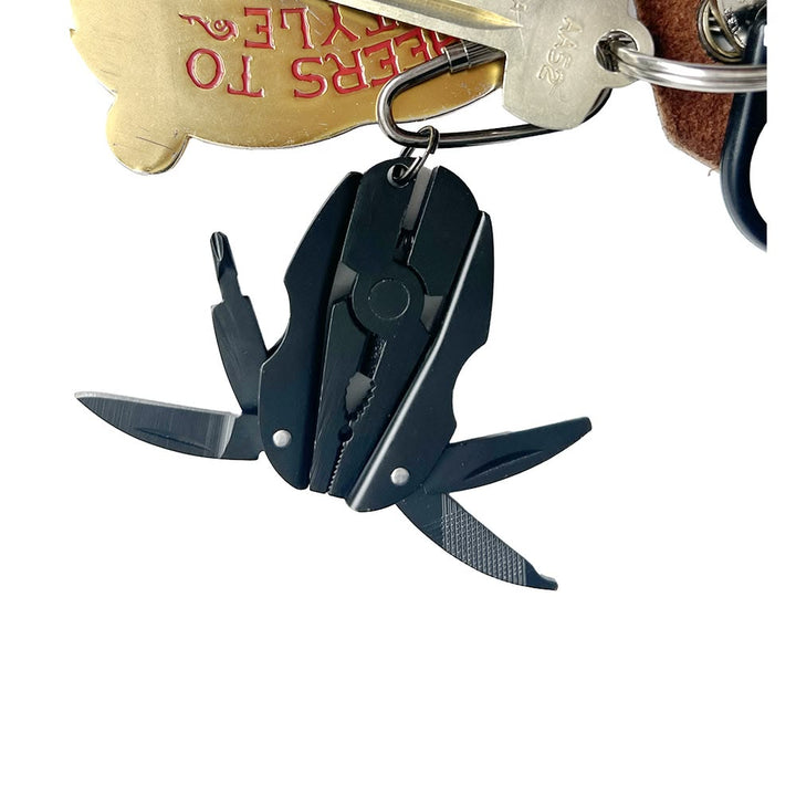 A black multi-tool keychain with several tools extended, attached to a keyring with keys and a gold-colored tag on a white background.