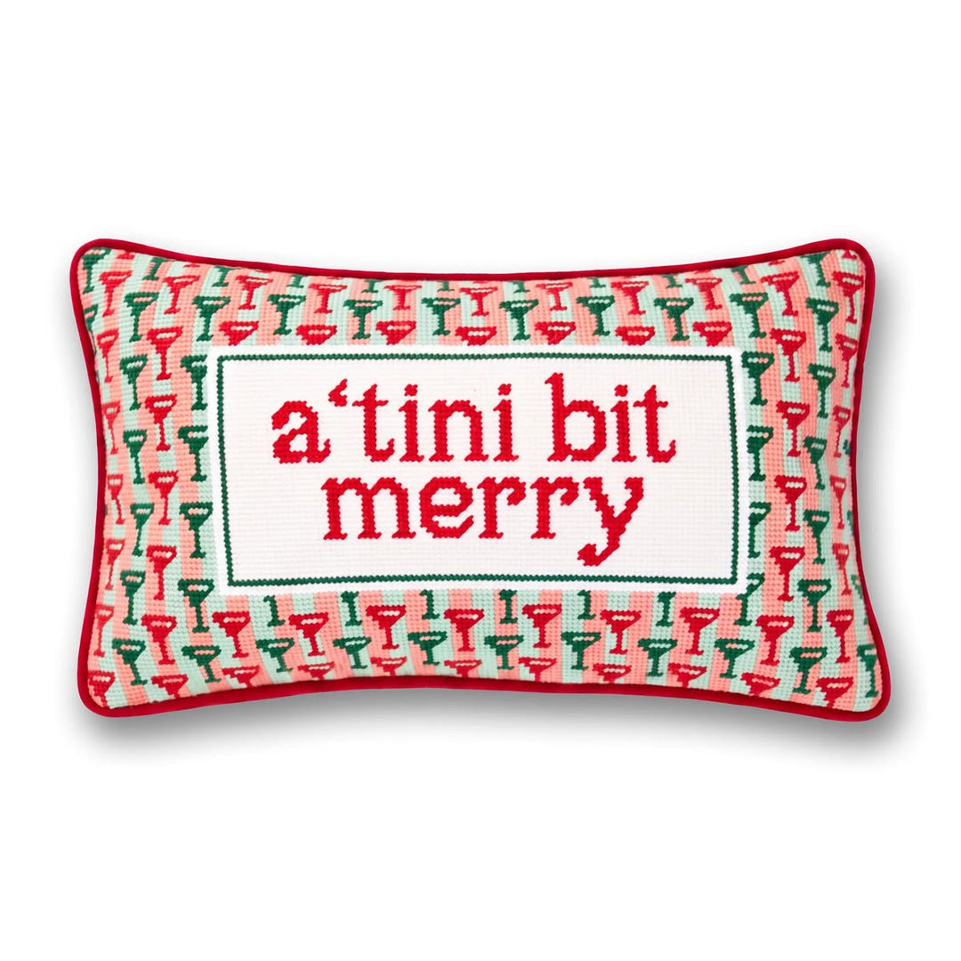 A rectangular decorative pillow with a red border and a white center panel reading 'a'tini bit merry' in red lettering, surrounded by a pattern of red and green cocktail glasses on a white background.