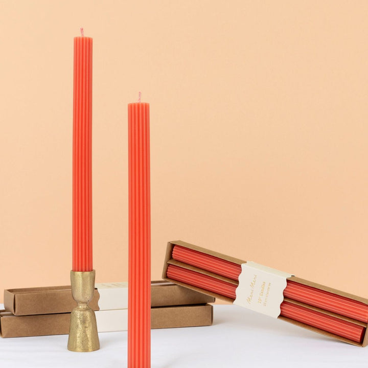 Two tall red candles with a gold holder and two boxes of red candles on a light beige background.
