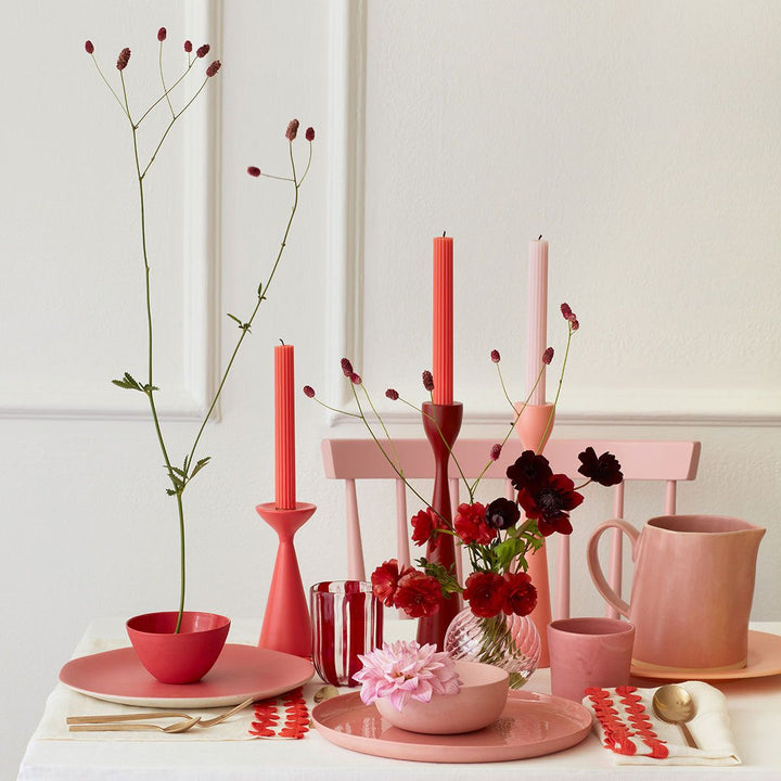 Pink tableware set with flowers and candles on a white surface