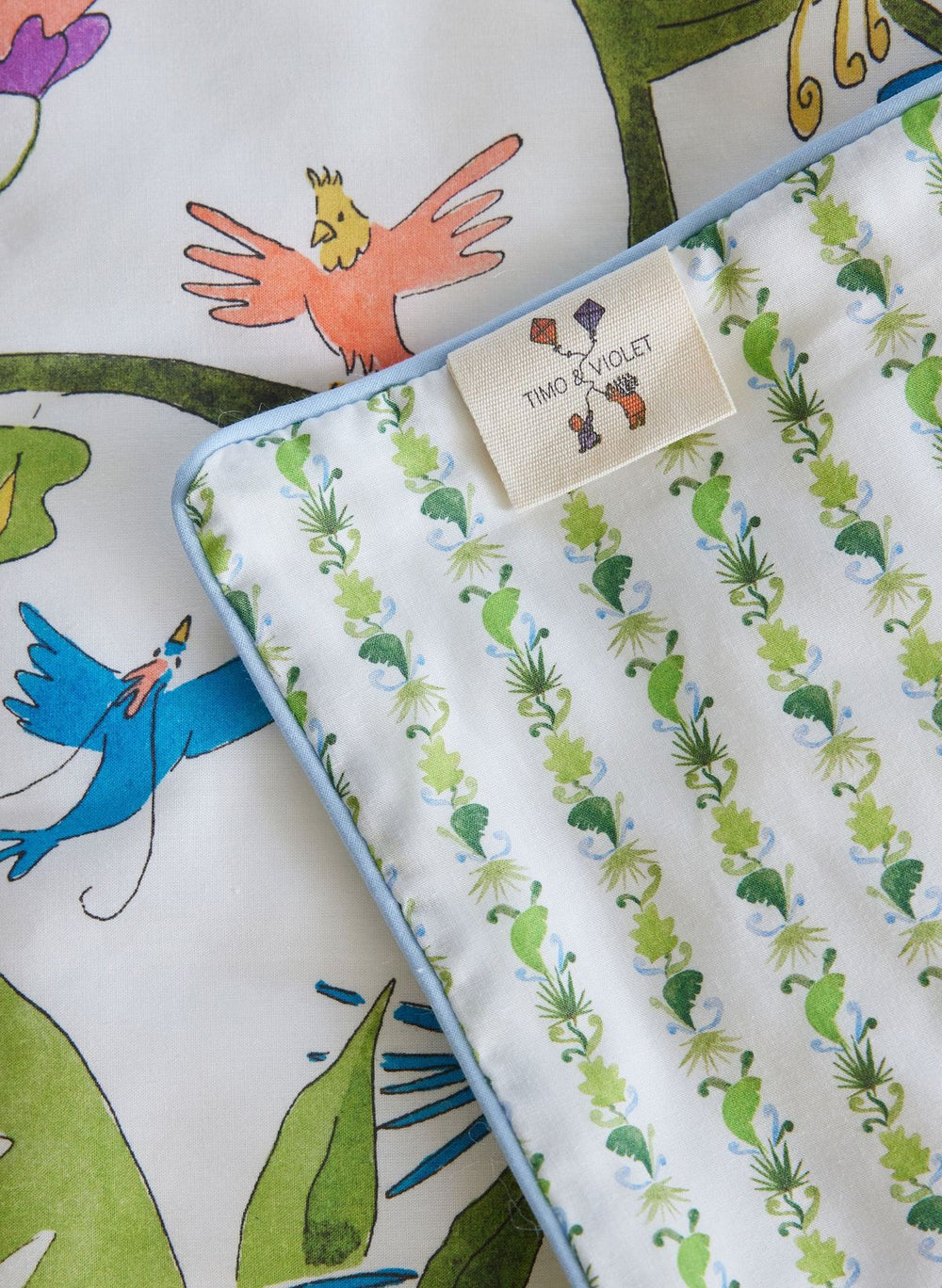Children's fabric with colorful bird and leaf pattern, featuring a brand tag.