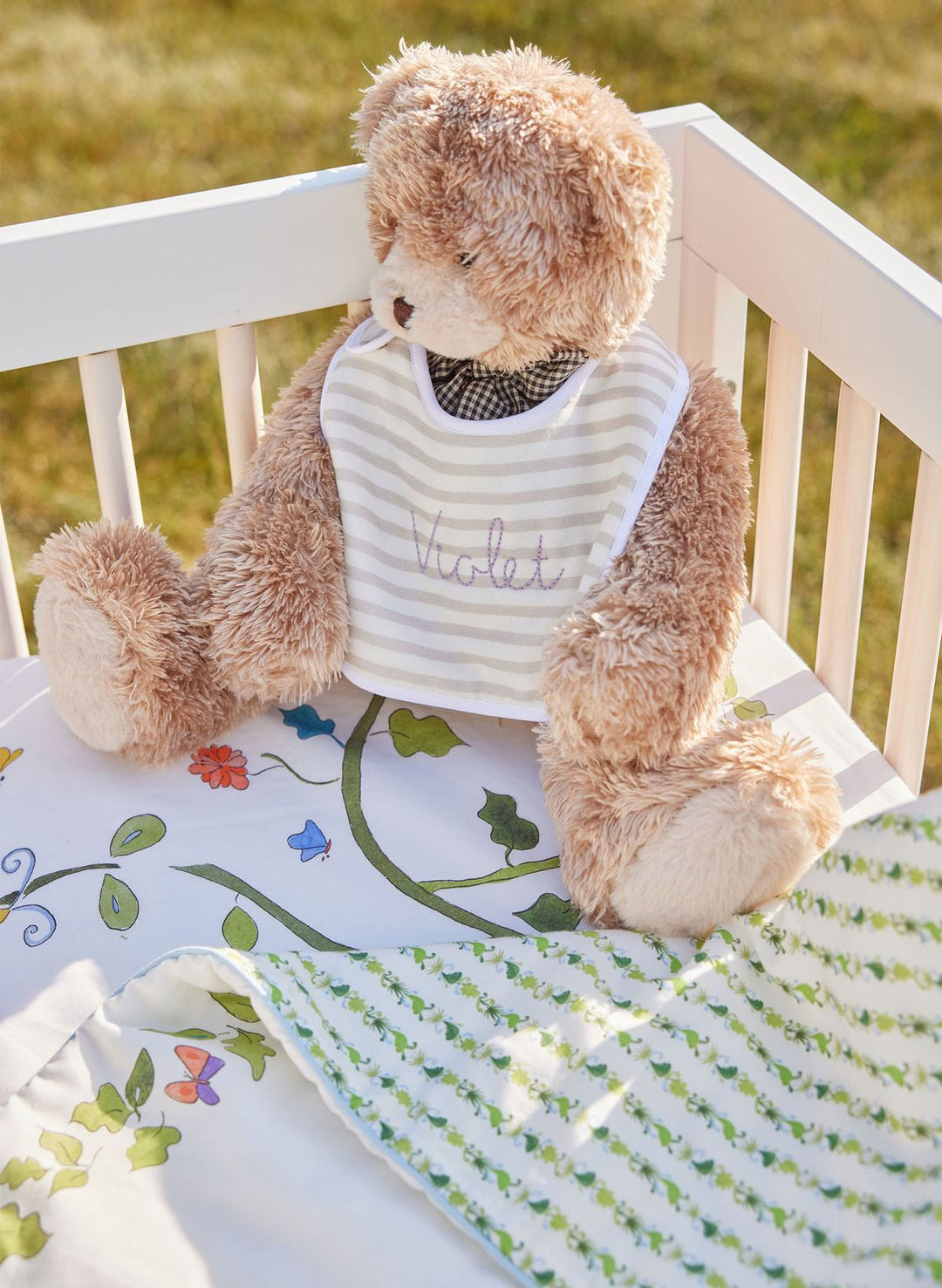 Teddy bear wearing a bib with 'Natalie' on it, sitting on a white bench outdoors.