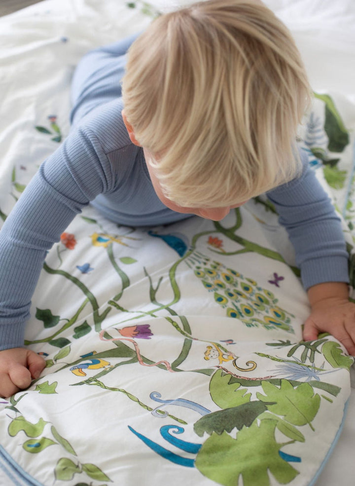 Child playing on a colorful play mat with nature-themed design