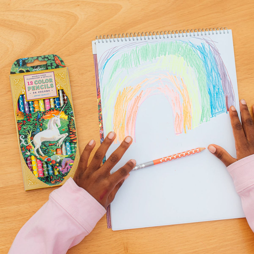 Child coloring a rainbow on a notebook with a box of color pencils on a wooden table