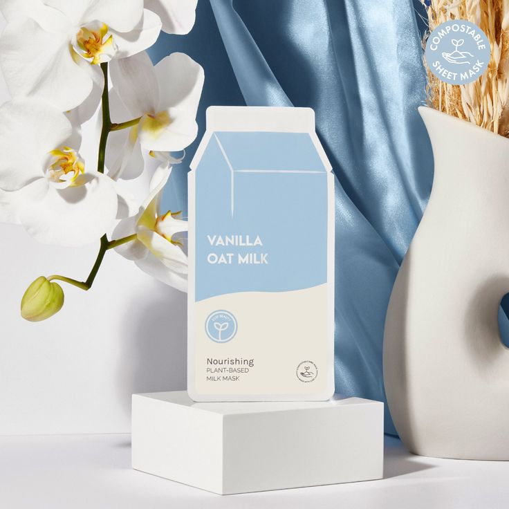Vanilla oat milk carton with white orchids and a blue curtain in the background