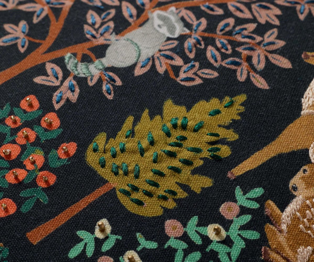Close-up of a fabric with embroidered design featuring animals and plants on a dark background.