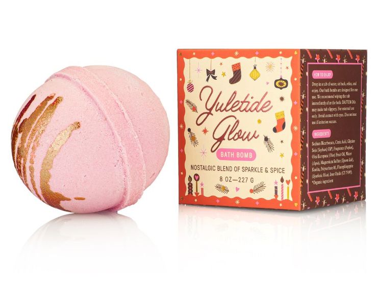 Pink bath bomb with gold accents next to its packaging on a white background